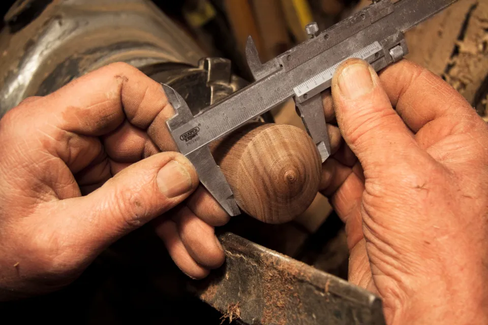 Les mains d'un artisan mesurant une pièce de bois dans son atelier